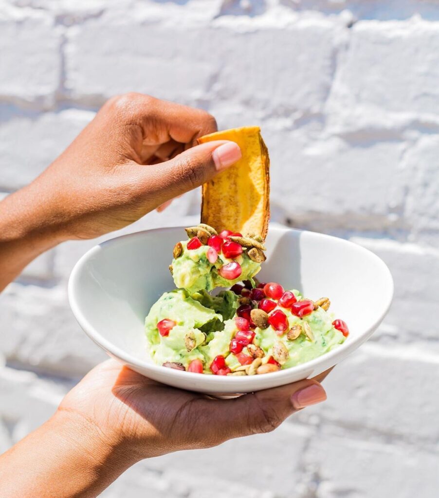 a hand dipping a plantain into a bowl of Tocaya guacamole