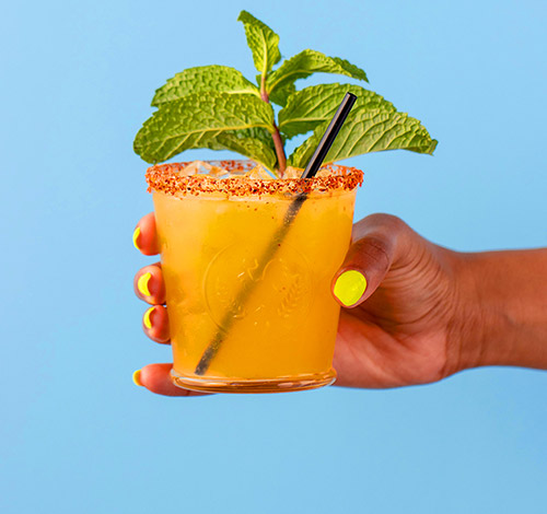hand holding a Tocaya margarita with mint sprig and straw
