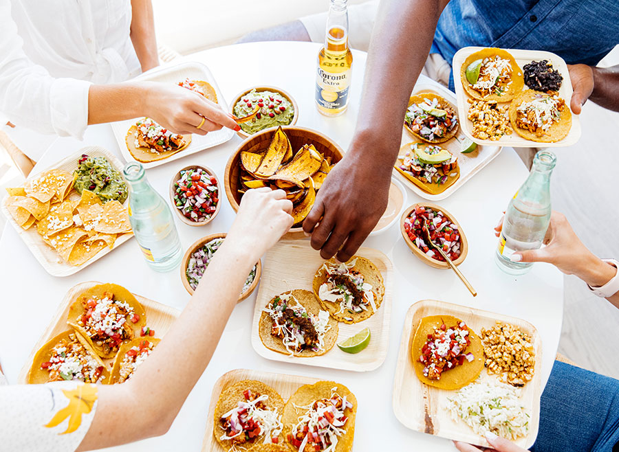 Aerial shot of four people sitting at a table with a variety of Tocaya food in front of them. Each of their hands are reaching for a different item to eat.